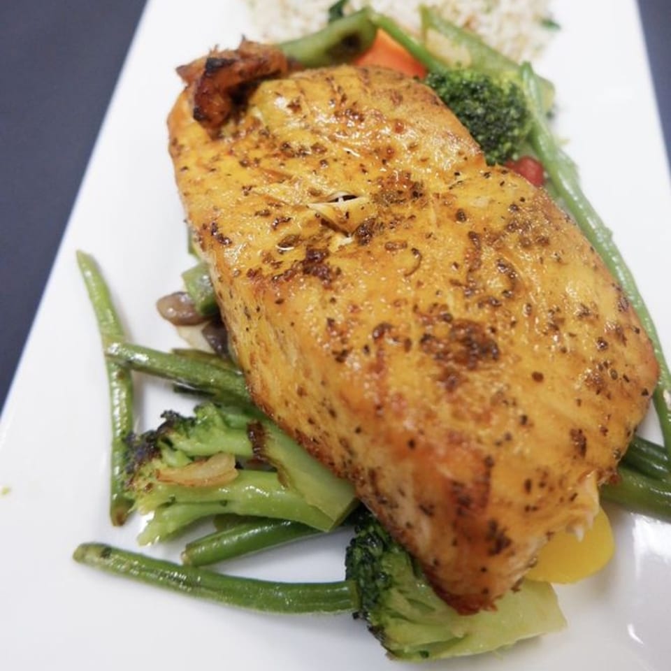 Indian Bistro's salmon fillet with green beans, broccoli, and rice on a white plate.