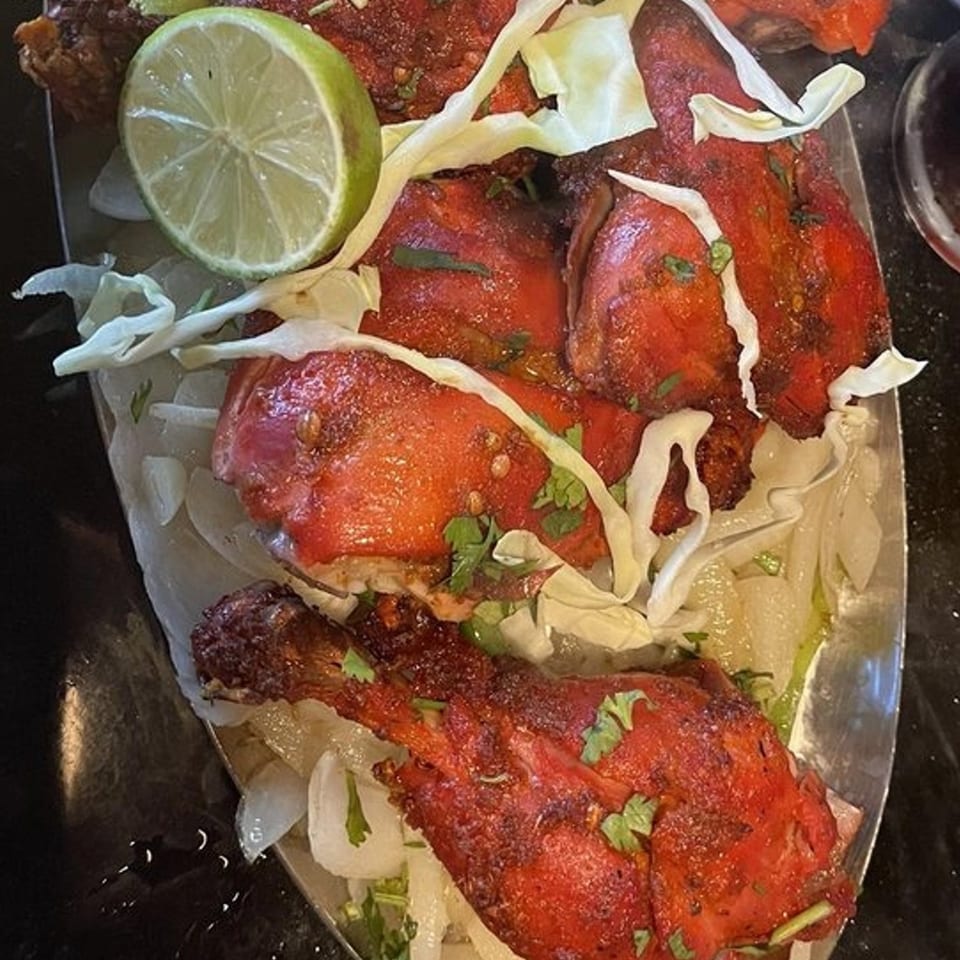 Indian Bistro's Tandoori Chicken, garnished with lime, cabbage, and cilantro on a silver platter.