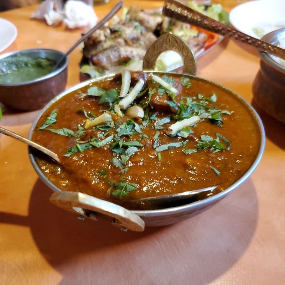 Indian Bistro's rich brown curry, garnished with fresh cilantro and ginger, in a metal bowl.